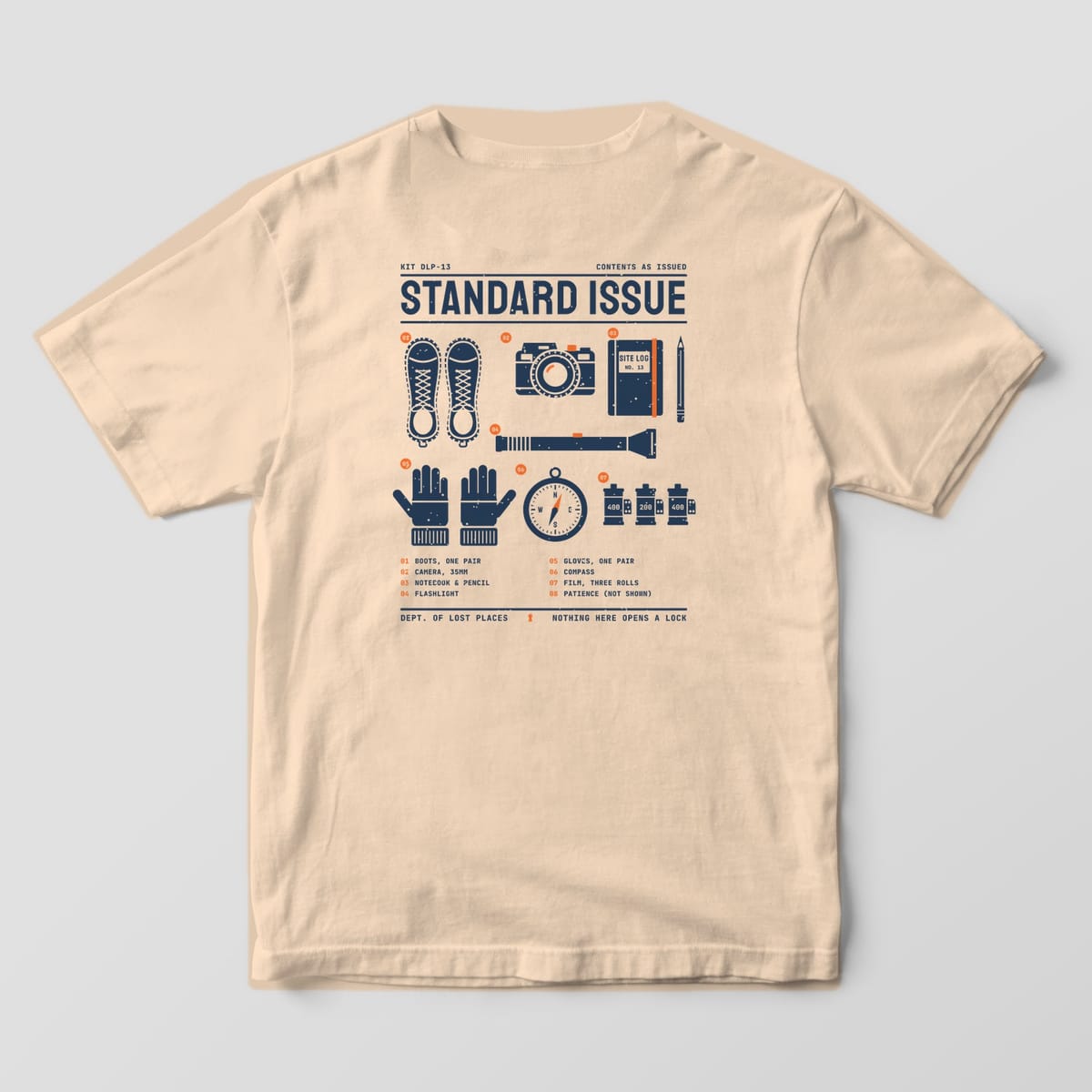 Back of an Ivory Comfort Colors 1717 tee printed with a navy and orange flat-lay of numbered explorer gear: boots, a film camera, a notebook and pencil, a flashlight, gloves, a compass and film rolls, under Standard Issue.