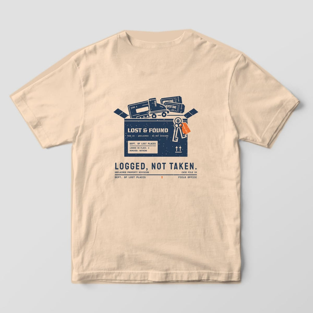 Back of an Ivory Comfort Colors 1717 tee printed with a navy lost and found cardboard box holding a cassette tape, a roller skate, ticket stubs and skeleton keys with an orange tag, above the words Logged, Not Taken.