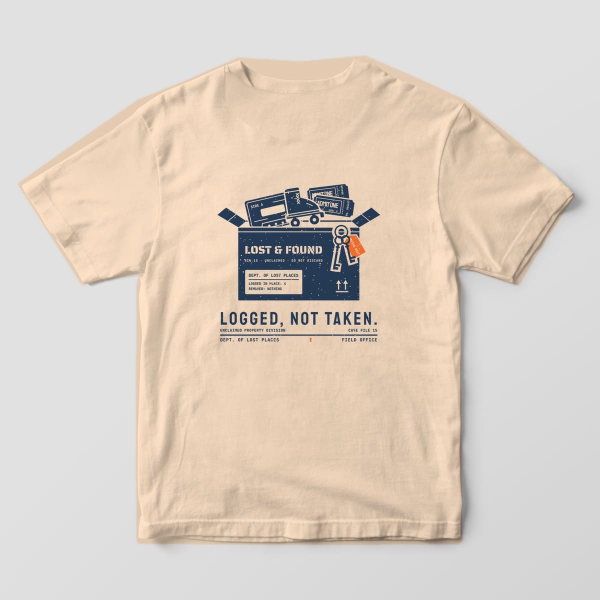 Back of an Ivory Comfort Colors 1717 tee printed with a navy lost and found cardboard box holding a cassette tape, a roller skate, ticket stubs and skeleton keys with an orange tag, above the words Logged, Not Taken.