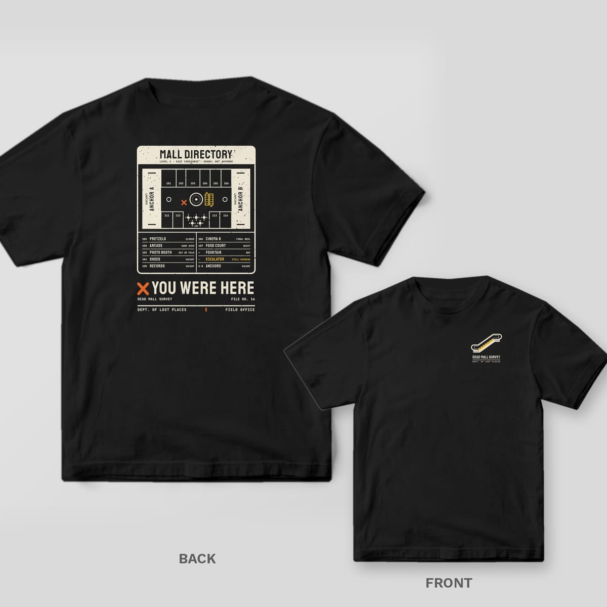 Black Comfort Colors tee shown back and front: the back has a cream dead mall directory map with an orange X above You Were Here; the chest has a small escalator.