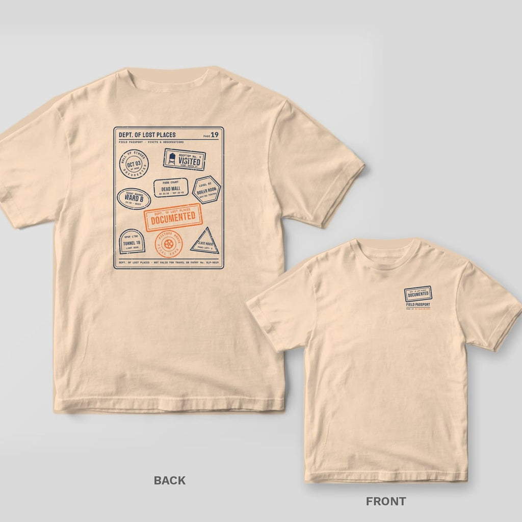 Ivory Comfort Colors tee shown back and front: the back has a navy passport page full of stamps from imaginary abandoned places with an orange Documented stamp; the chest has a small Documented stamp.