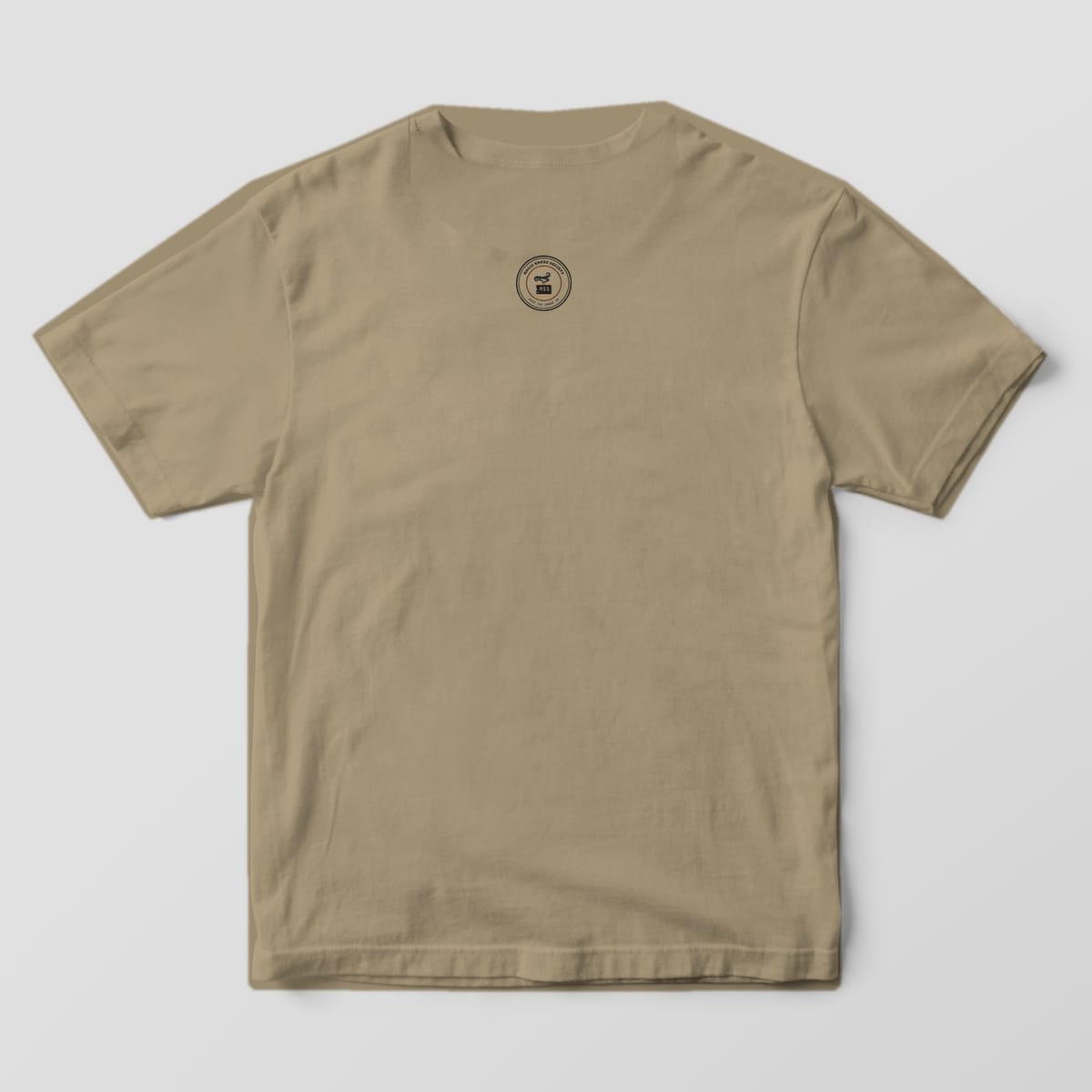 Back of a khaki Comfort Colors 1717 tee with a small round Magic Smoke Society seal below the collar.