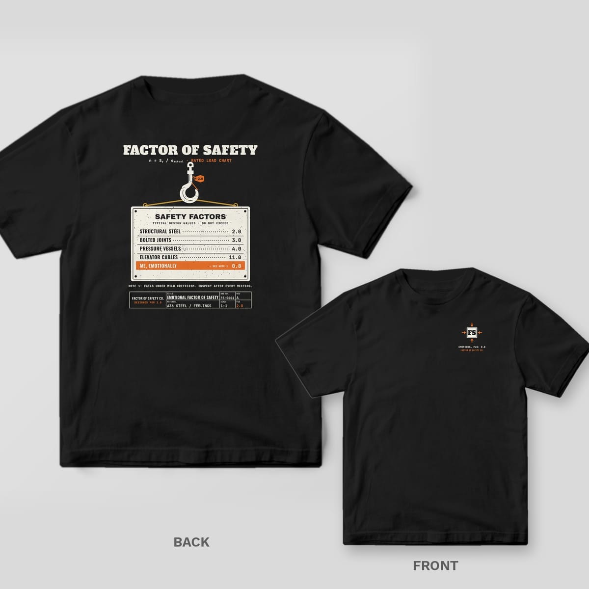 Black tee shown back and front: the back has a crane hook lifting a cream safety-factors chart with an orange Me, Emotionally 0.8 row; the front has a small FS monogram with four orange force arrows on the left chest.
