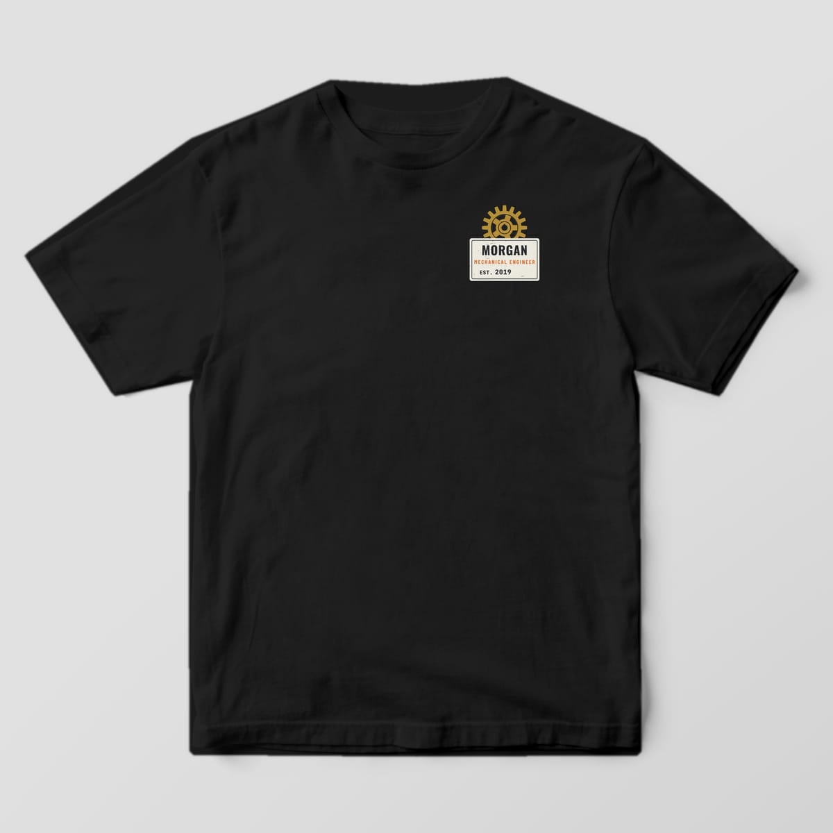 Front of a black Comfort Colors 1717 tee with a small personalized data plate with a brass gear on the left chest.