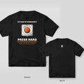 Black tee shown front and back: front has a large orange emergency stop button under In Case of Emergency with Press Hard below; back has a small e-stop at the neck.