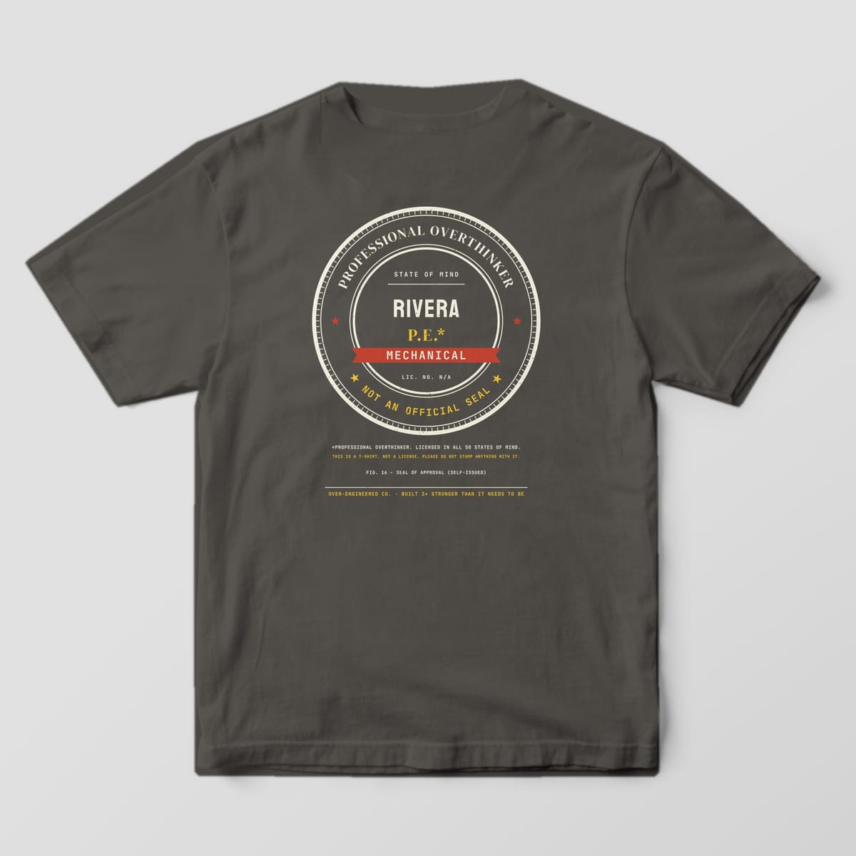 Back of a pepper Comfort Colors 1717 tee with a large round Professional Overthinker seal with the sample name RIVERA and MECHANICAL.