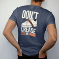 Man wearing a Navy tee, seen from the back: a clean sneaker toe box wrapped in caution tape with Don't above and Crease Me below, as a two-ink streetwear graphic in off-white and orange.