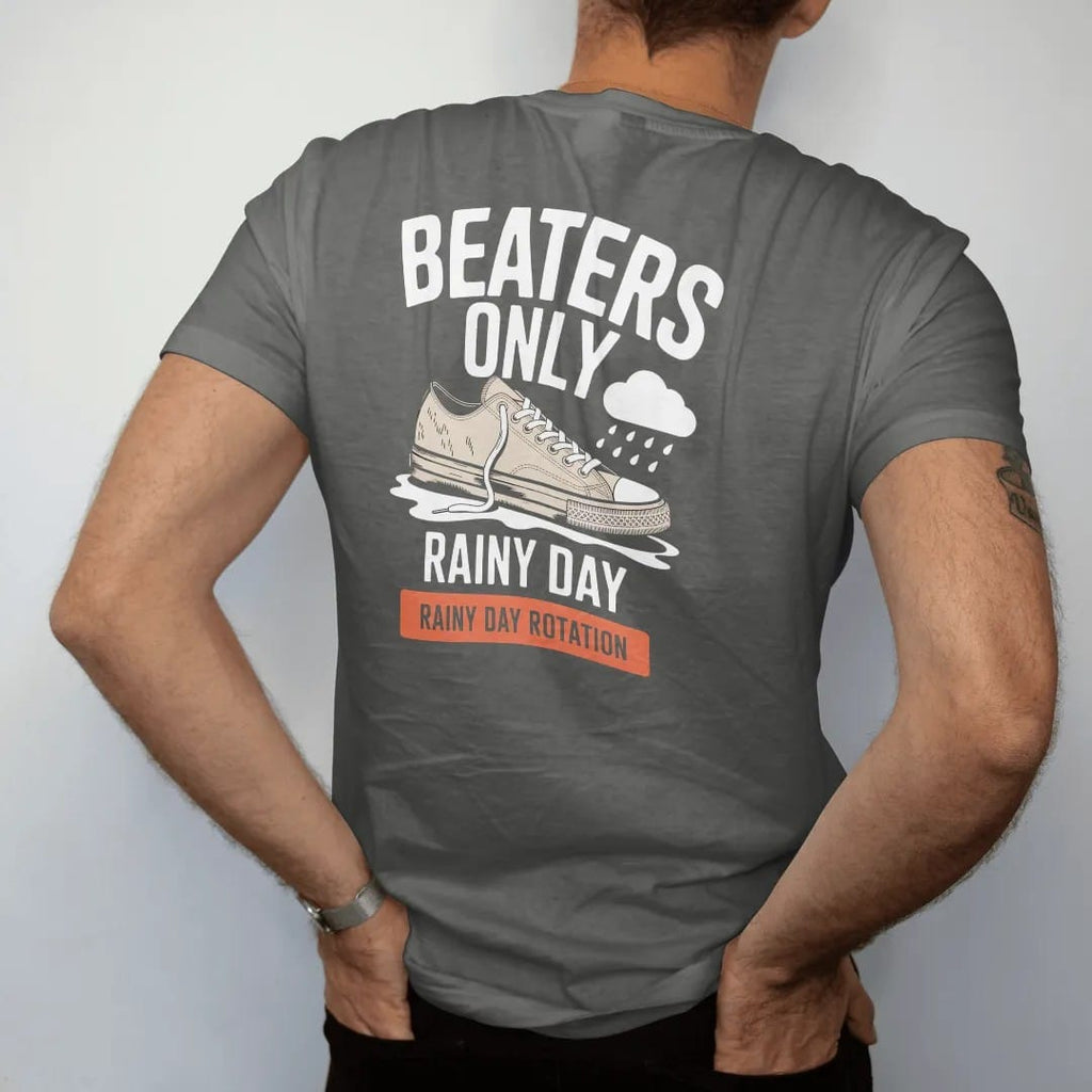 Man wearing a Pepper tee, seen from the back: a scuffed sneaker with a frayed lace splashing a puddle under a rain cloud, labeled Beaters Only and Rainy Day Rotation, as a two-ink streetwear graphic in off-white and orange.