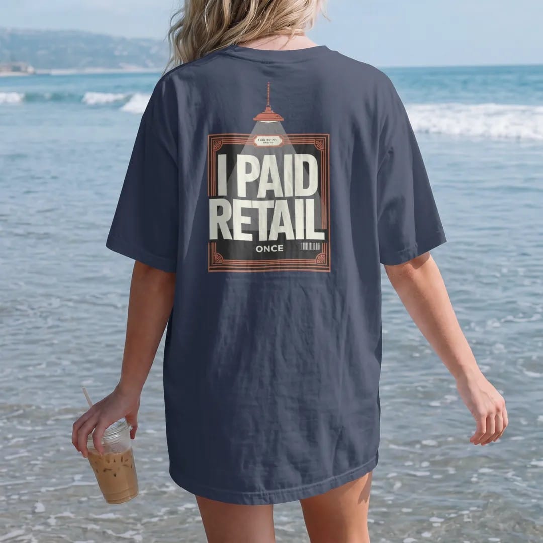 Woman on the beach in a Navy tee, back view: a receipt framed on a wall under a spotlight with a velvet rope, plaque reading I Paid Retail and Once below, as a two-ink streetwear graphic in off-white and orange.