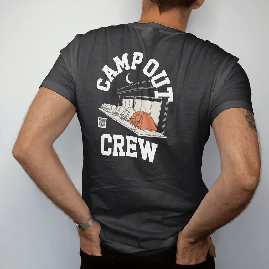 Man wearing a Black tee, seen from the back: tents and folding chairs lined up outside a shop under a crescent moon, with Camp Out arched over Crew, as a two-ink streetwear graphic in off-white and orange.