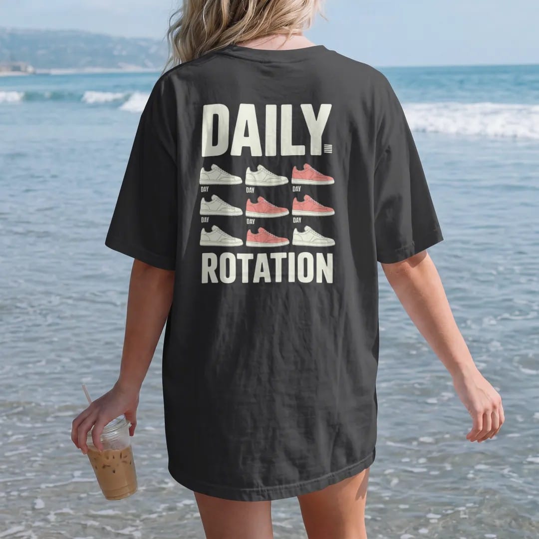 Woman on the beach in a Black tee, back view: a weekly planner grid of seven different sneakers under Daily and above a big Rotation, as a two-ink streetwear graphic in off-white and orange.