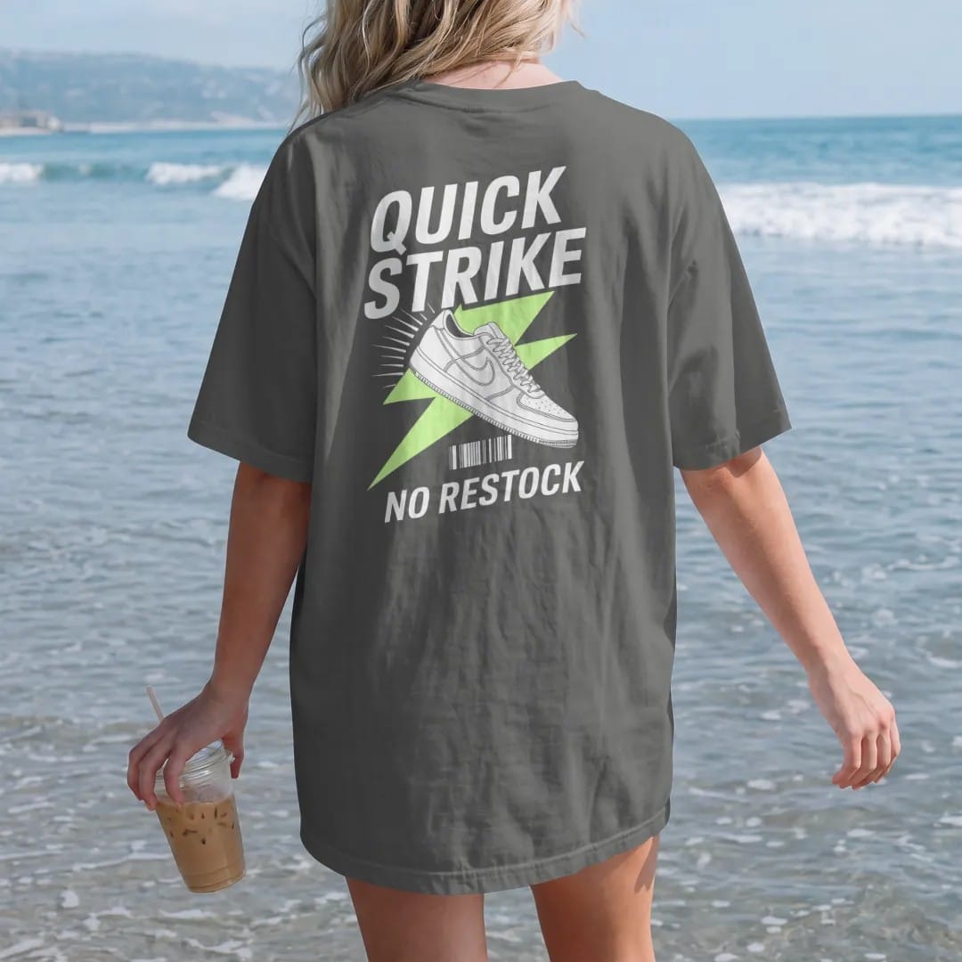 Woman on the beach in a Pepper tee, back view: a sneaker bursting through a lightning bolt with speed lines under Quick Strike and stamped No Restock, as a two-ink streetwear graphic in off-white and lime.