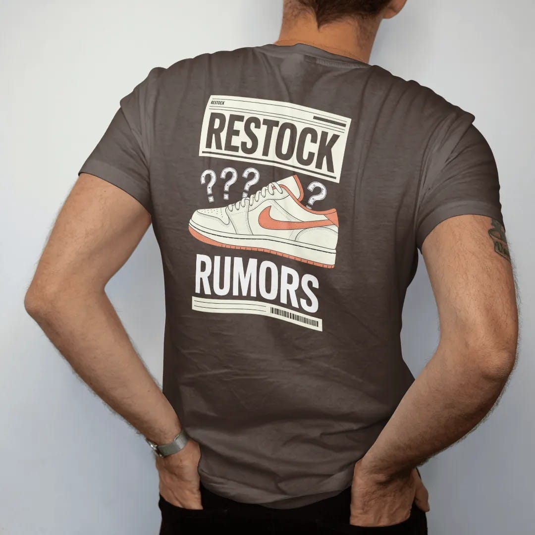 Man wearing a Espresso tee, seen from the back: a vintage newspaper page with a sneaker photo and scribbled arrows, masthead Restock and headline Rumors, as a two-ink streetwear graphic in off-white and orange.