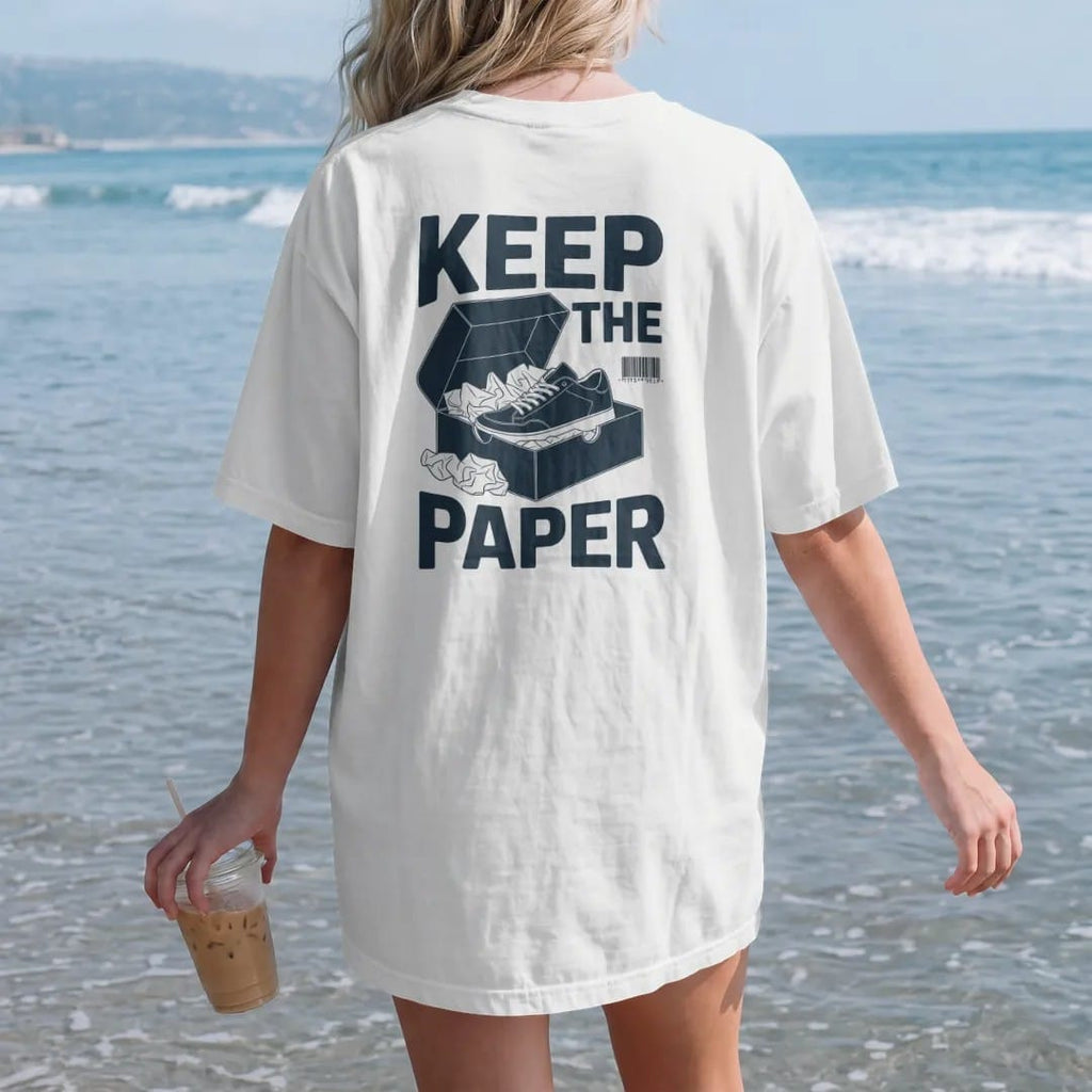Woman on the beach in a White tee, back view: an open shoebox overflowing with crumpled tissue paper and a nested sneaker, under Keep The and above Tissue Paper, as a two-ink streetwear graphic in navy and orange.