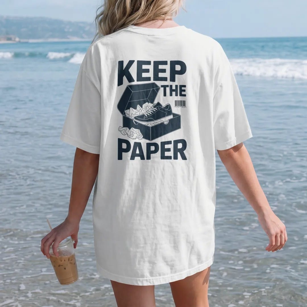 Woman on the beach in a White tee, back view: an open shoebox overflowing with crumpled tissue paper and a nested sneaker, under Keep The and above Tissue Paper, as a two-ink streetwear graphic in navy and orange.