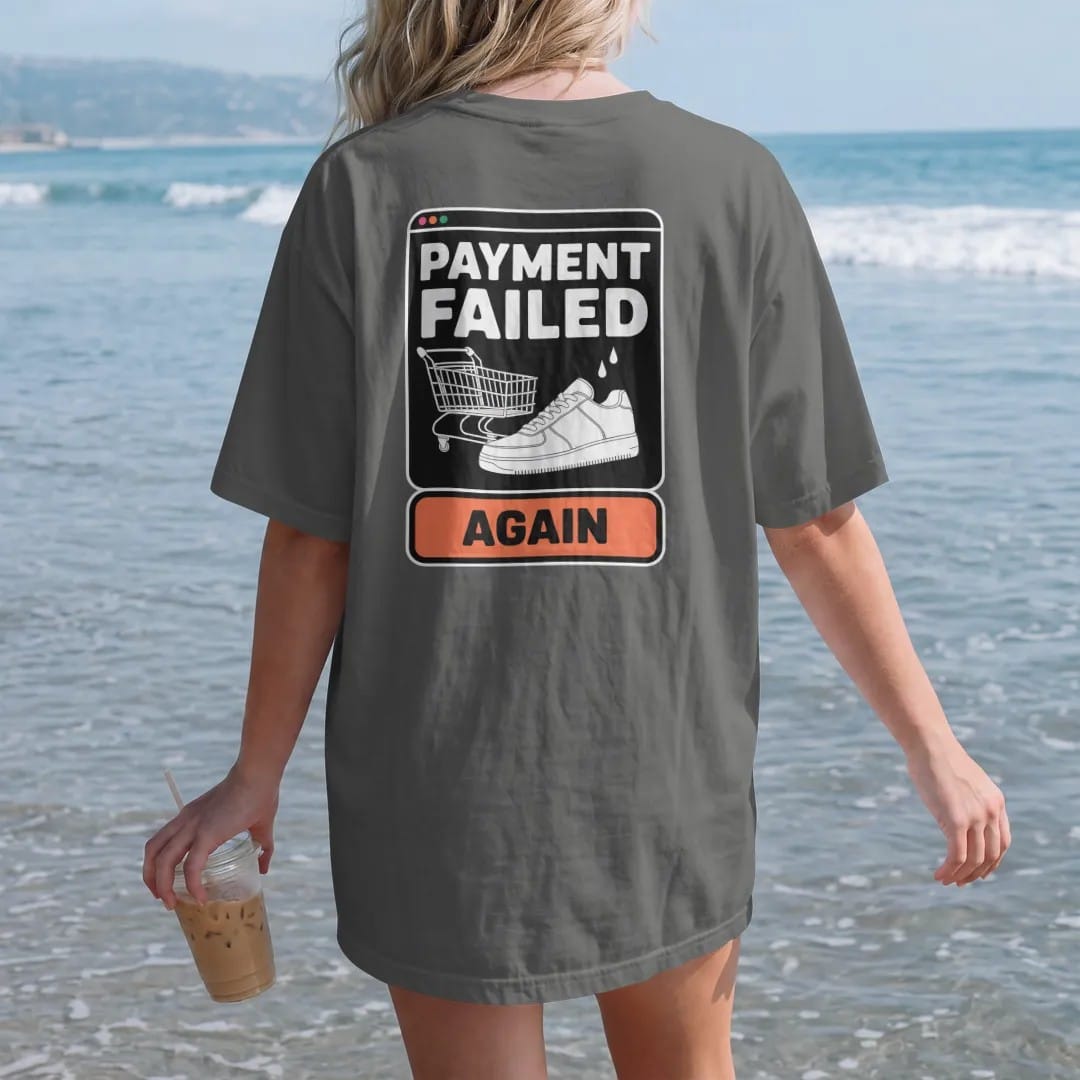 Woman on the beach in a Pepper tee, back view: a retro error pop-up with a broken cart and sweating sneaker, titled Payment Failed with an Again button, as a two-ink streetwear graphic in off-white and orange.