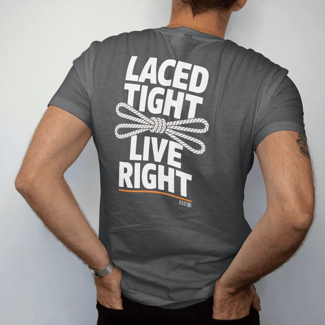 Man wearing a Graphite tee, seen from the back: a close-up of sneaker eyelets with a tidy bow knot framed by Laced Tight and Live Right, as a two-ink streetwear graphic in off-white and orange.