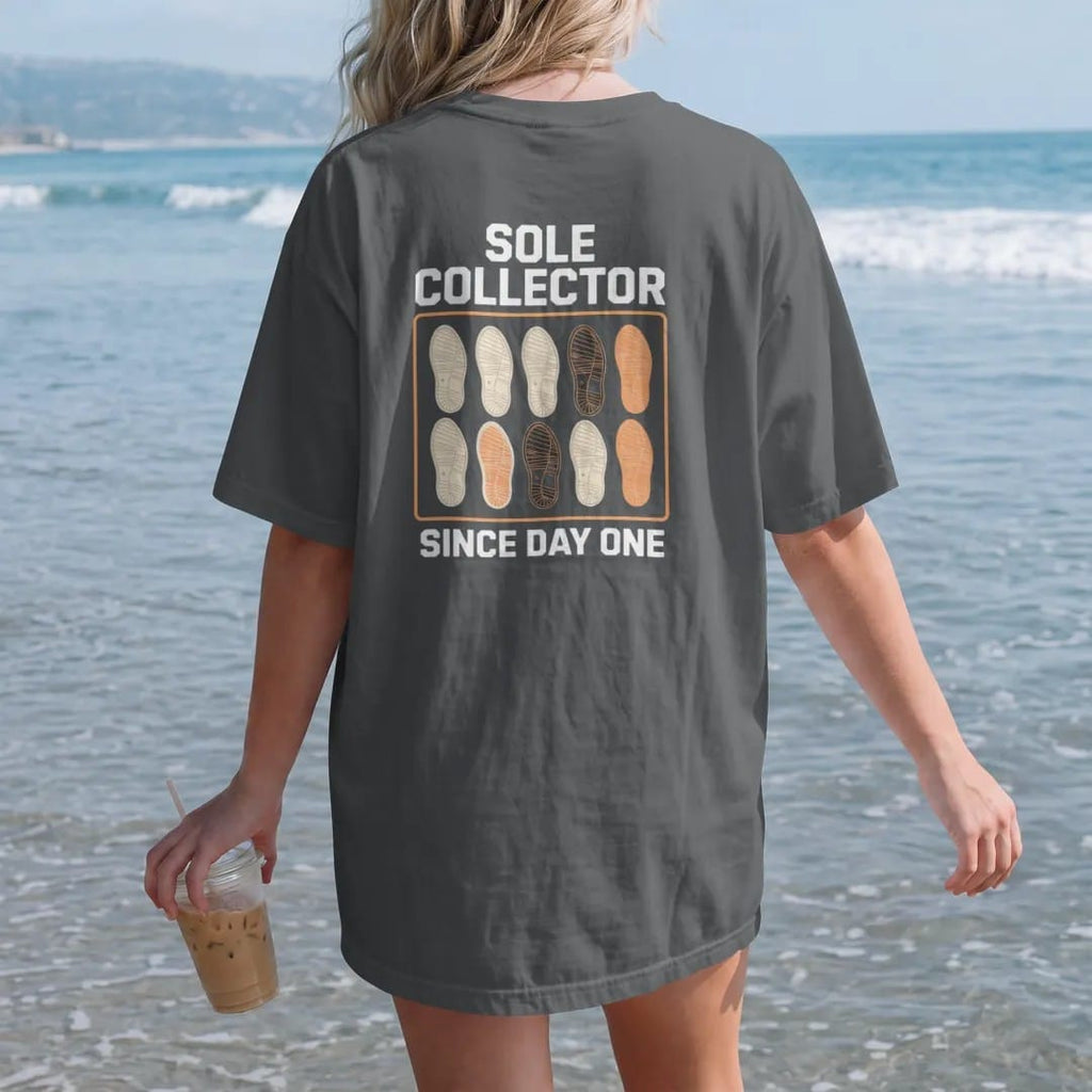 Woman on the beach in a Graphite tee, back view: a specimen board pinning sneaker outsoles like butterflies under Sole Collector and Since Day One, as a two-ink streetwear graphic in off-white and orange.