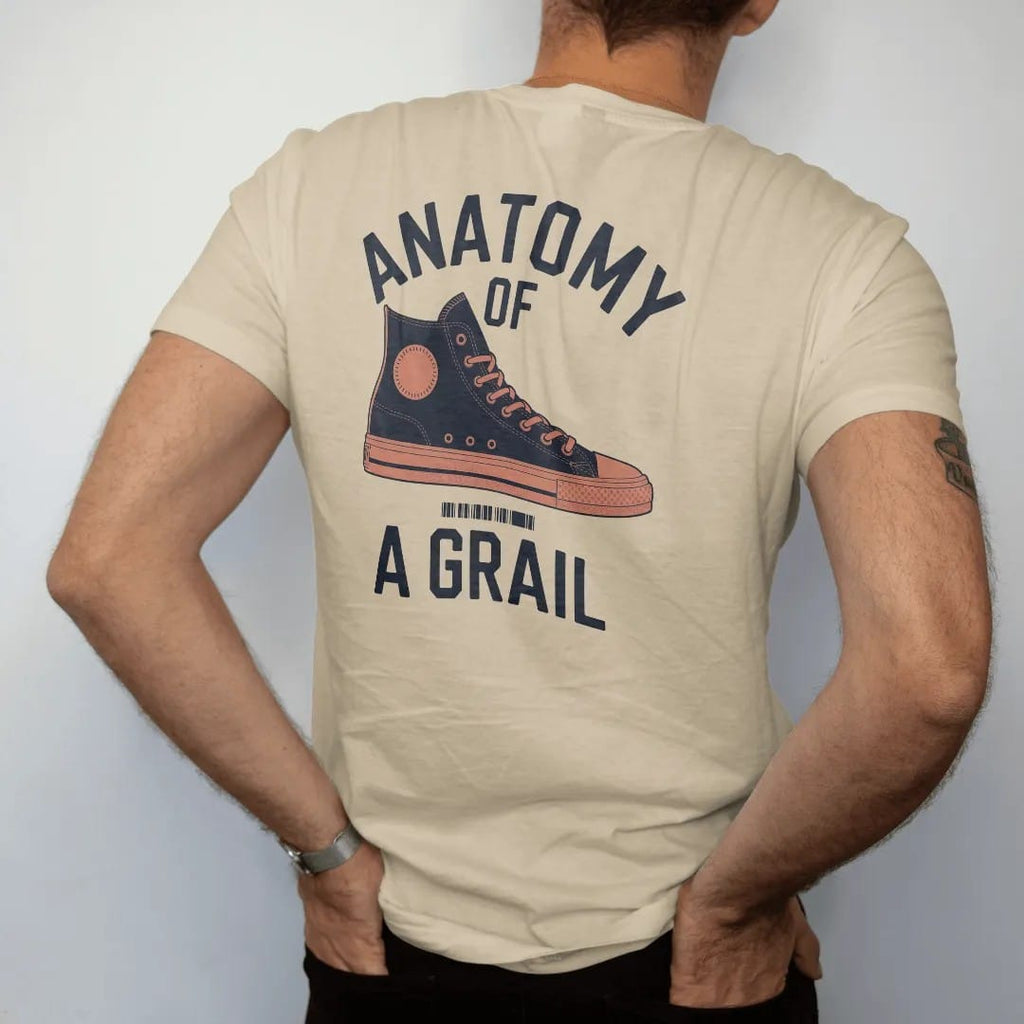 Man wearing a Sandstone tee, seen from the back: an exploded diagram of a high-top sneaker with leader lines under Anatomy Of and above A Grail, as a two-ink streetwear graphic in navy and orange.