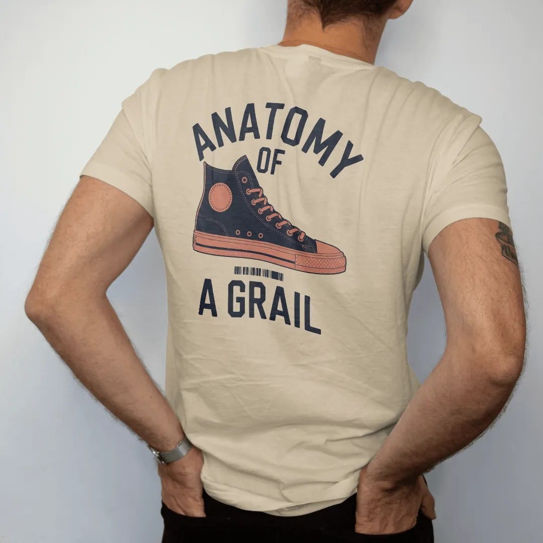 Man wearing a Sandstone tee, seen from the back: an exploded diagram of a high-top sneaker with leader lines under Anatomy Of and above A Grail, as a two-ink streetwear graphic in navy and orange.