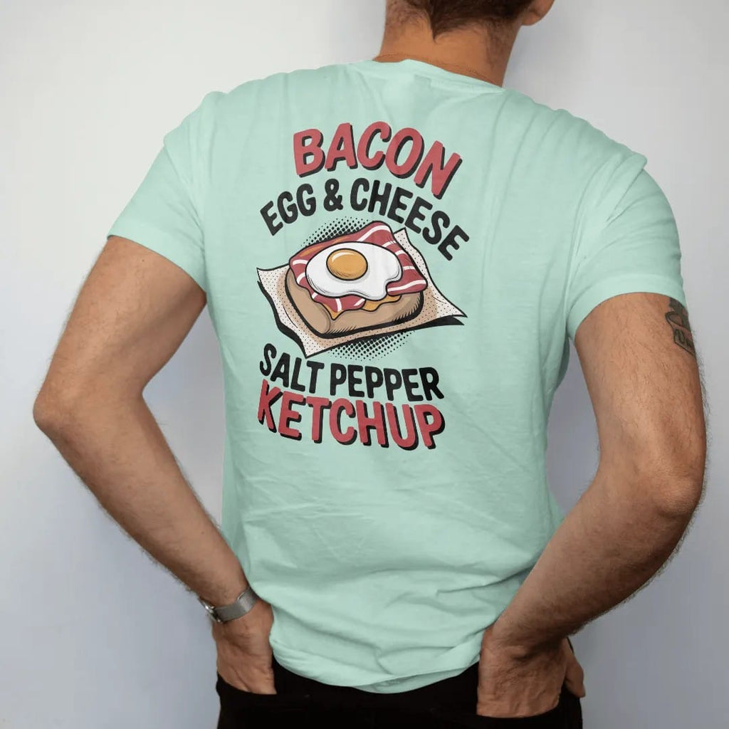 Man wearing a Chalky Mint tee, seen from the back: a bacon egg and cheese on a roll in deli paper with Bacon Egg & Cheese stacked above Salt Pepper Ketchup, in halftone comic-pop red, mustard and navy.
