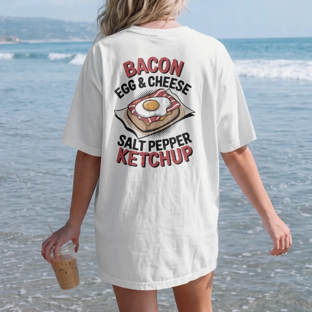Woman on the beach in a White tee, back view: a bacon egg and cheese on a roll in deli paper with Bacon Egg & Cheese stacked above Salt Pepper Ketchup, in halftone comic-pop red, mustard and navy.