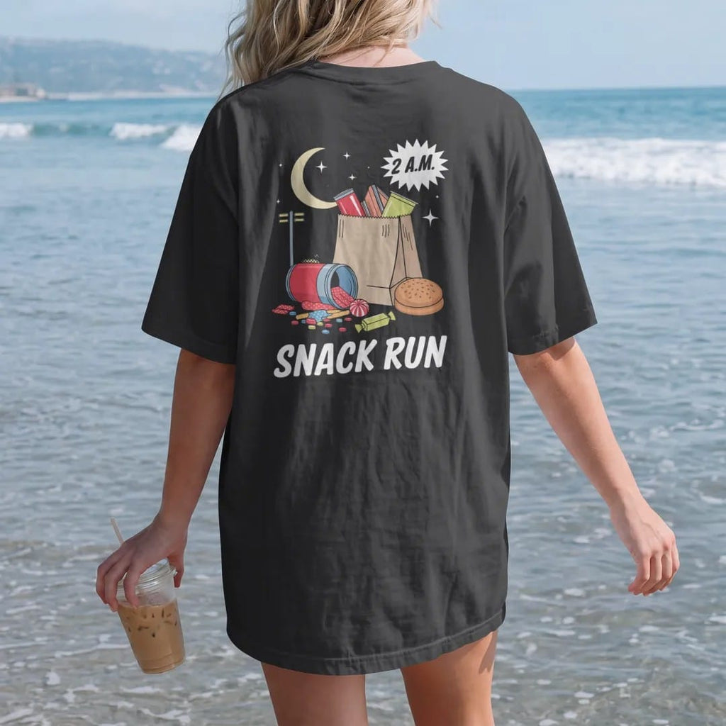 Woman on the beach in a Black tee, back view: a paper bag spilling chips, soda, candy and a honey bun under a crescent moon and streetlight, with 2 A.M. and Snack Run, in halftone comic-pop red, yellow and cream.