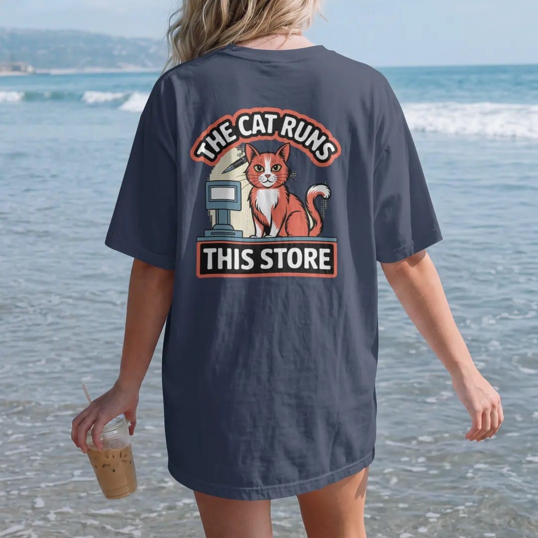 Woman on the beach in a Navy tee, back view: an orange cat behind a register with a pen behind its ear, framed by The Cat Runs and This Store, in halftone comic-pop red, yellow and cream.