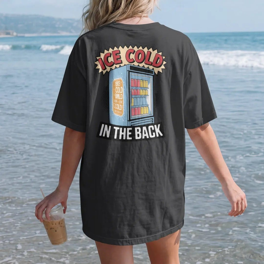 Woman on the beach in a Black tee, back view: a frosty glass-door drink fridge full of cans with Ice Cold in frosted letters and In The Back below, in halftone comic-pop red, yellow and cream.