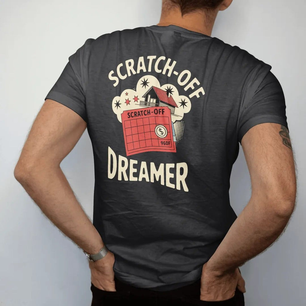 Man wearing a Black tee, seen from the back: a half-scratched ticket revealing stars and a coin under a dream cloud of a beach house, with Scratch-Off and Dreamer, in halftone comic-pop red, yellow and cream.