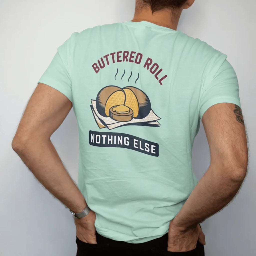 Man wearing a Chalky Mint tee, seen from the back: a split roll with melting butter on deli paper with steam, under Buttered Roll and Nothing Else, in halftone comic-pop red, mustard and navy.