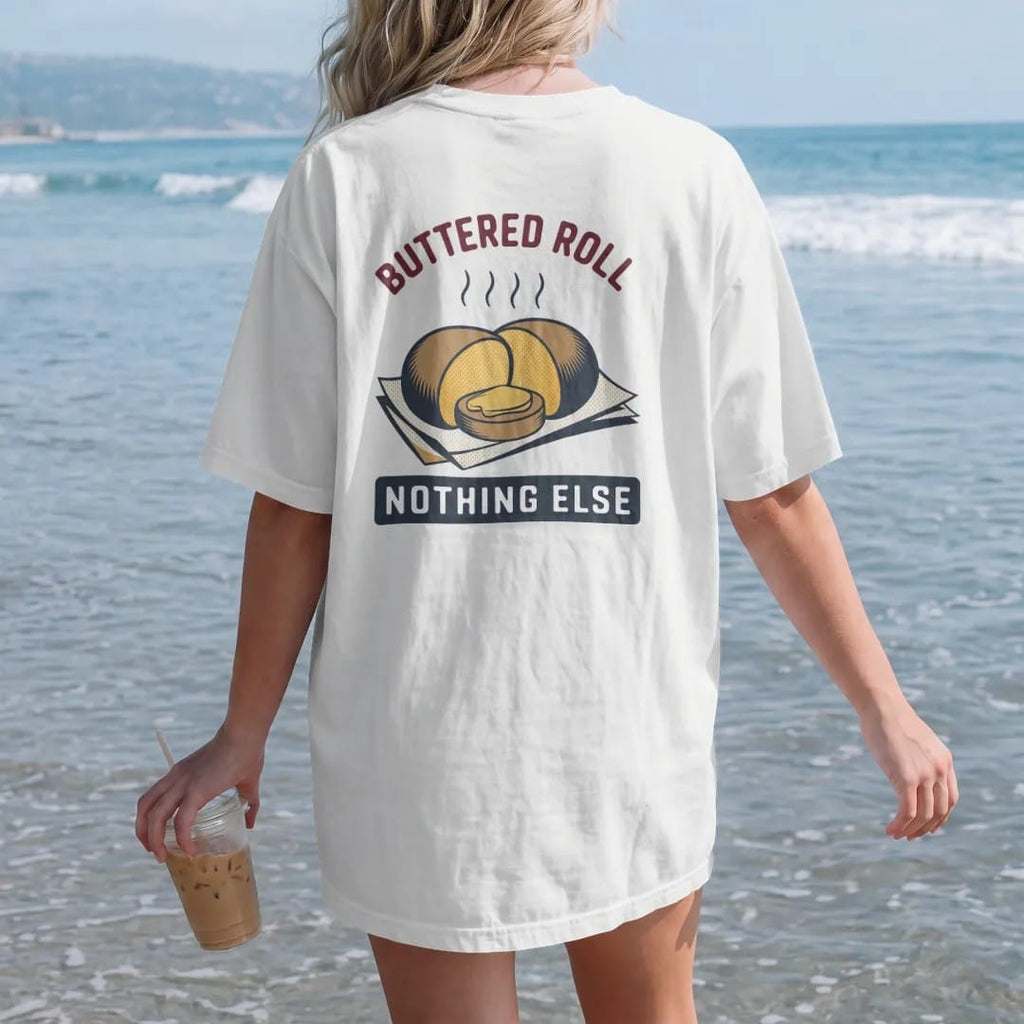 Woman on the beach in a White tee, back view: a split roll with melting butter on deli paper with steam, under Buttered Roll and Nothing Else, in halftone comic-pop red, mustard and navy.