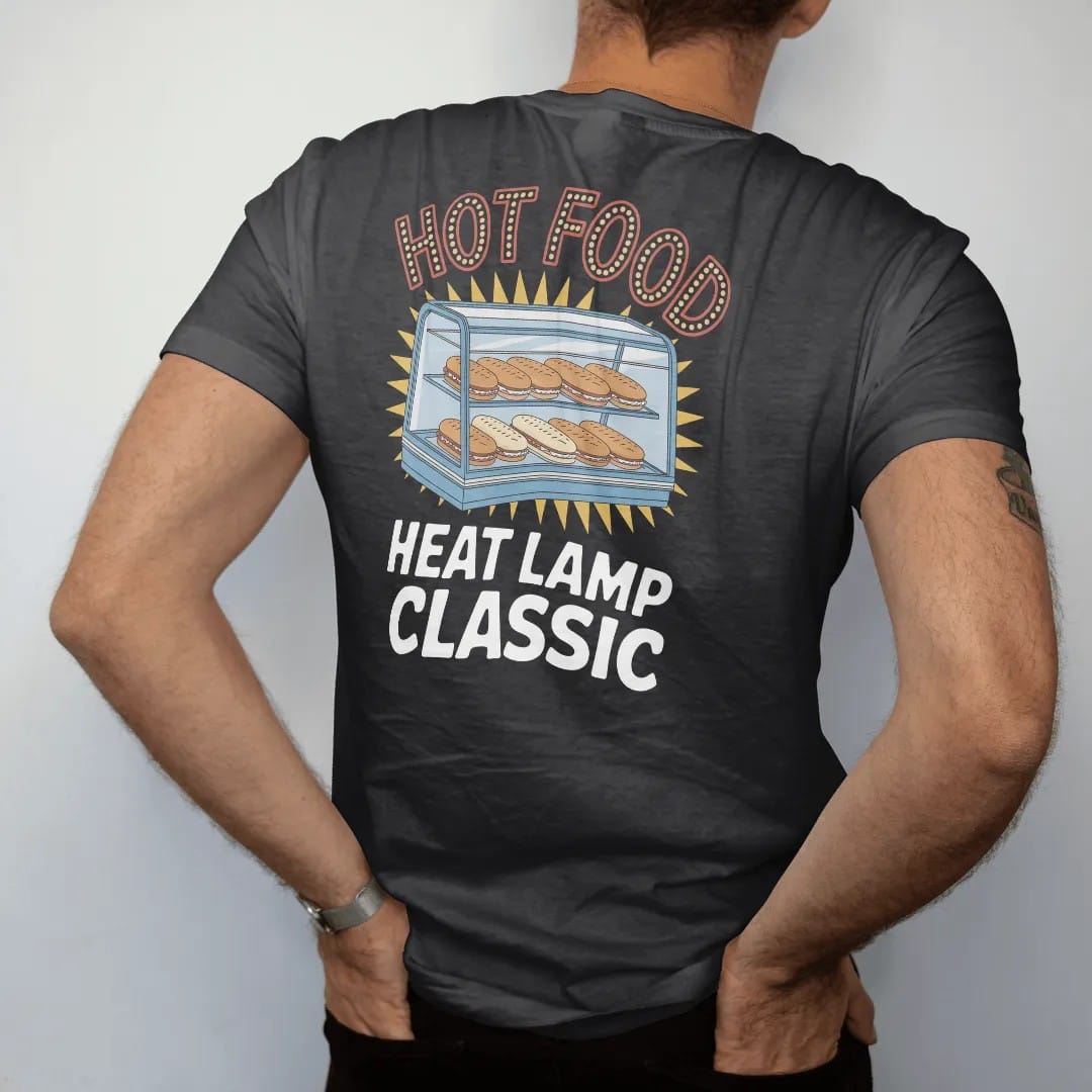 Man wearing a Black tee, seen from the back: a glass warmer case under glowing heat lamps with foil-wrapped food, under neon Hot Food and Heat Lamp Classic, in halftone comic-pop red, yellow and cream.