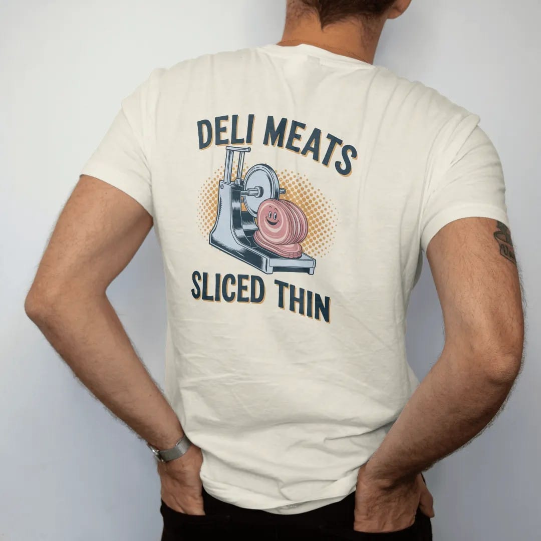 Man wearing a Ivory tee, seen from the back: a vintage ad of a chrome slicer cutting ham with a smiling slice, under a Deli Meats banner and Sliced Thin script, in halftone comic-pop red, mustard and navy.