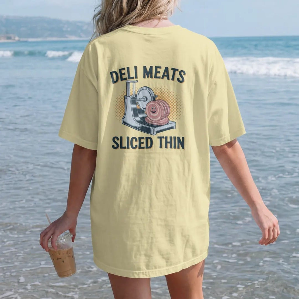 Woman on the beach in a Butter tee, back view: a vintage ad of a chrome slicer cutting ham with a smiling slice, under a Deli Meats banner and Sliced Thin script, in halftone comic-pop red, mustard and navy.