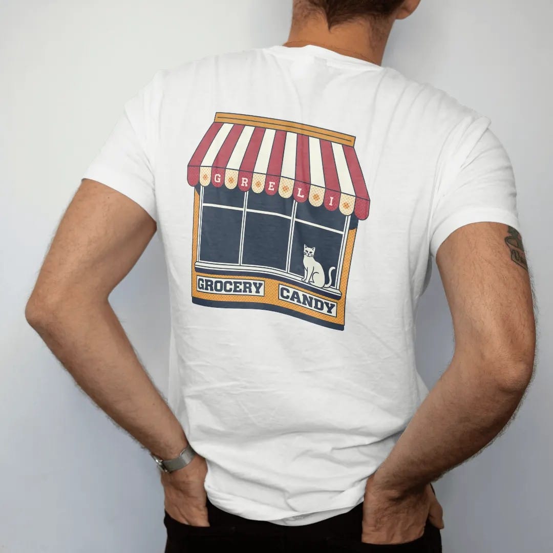 Man wearing a White tee, seen from the back: a striped scalloped awning painted with Grocery, Deli and Candy over a cat on a windowsill, in halftone comic-pop red, mustard and navy.