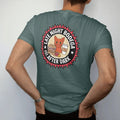 Man wearing a Blue Spruce tee, seen from the back: a round badge with an orange cat flanked by a sandwich and coffee cup, ringed by Late Night Bodega and Est. After Dark, in halftone comic-pop red, yellow and cream.
