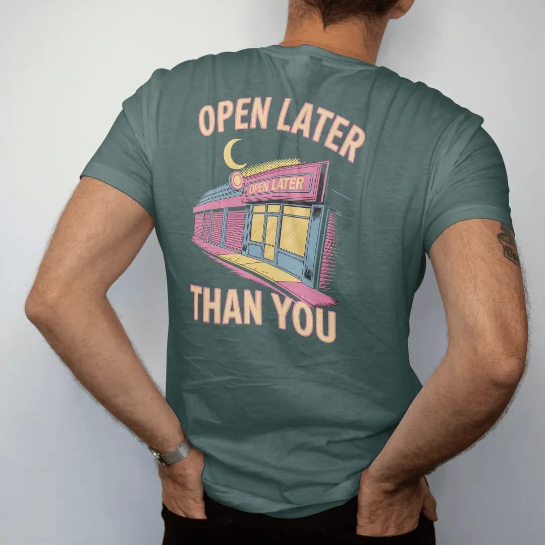 Man wearing a Blue Spruce tee, seen from the back: a lit storefront under a crescent moon on a street of closed shutters, with neon Open Later and Than You, in halftone comic-pop pink, yellow and cream.