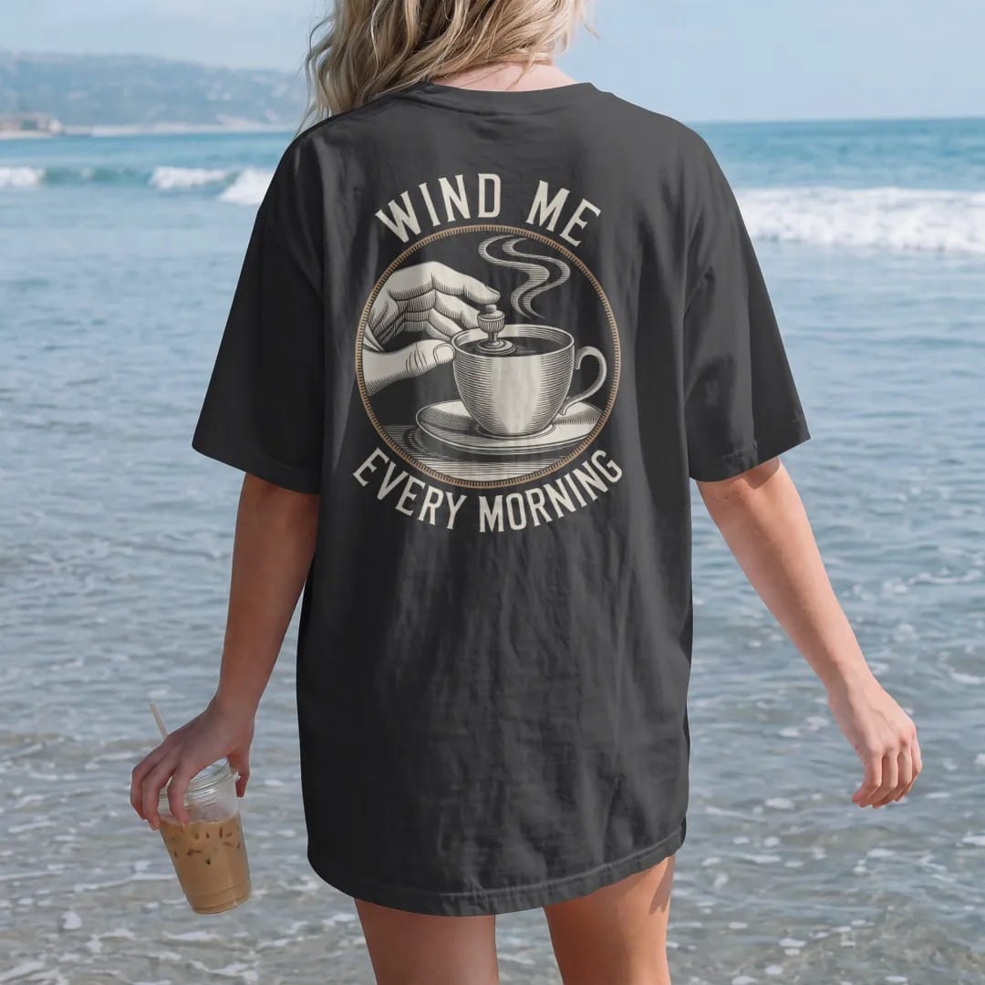 Woman on the beach in a Black tee, back view: fingers turning a watch winding crown with curved arrows and a steaming coffee cup, under Wind Me and Every Morning, as a fine engraving in antique gold and cream.