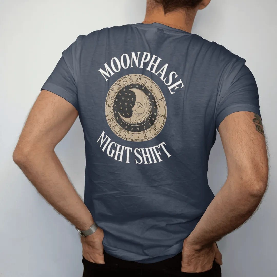 Man wearing a Midnight tee, seen from the back: a moonphase window with an engraved smiling moon on a starry disc, under Moonphase and Night Shift, as a fine engraving in antique gold and cream.