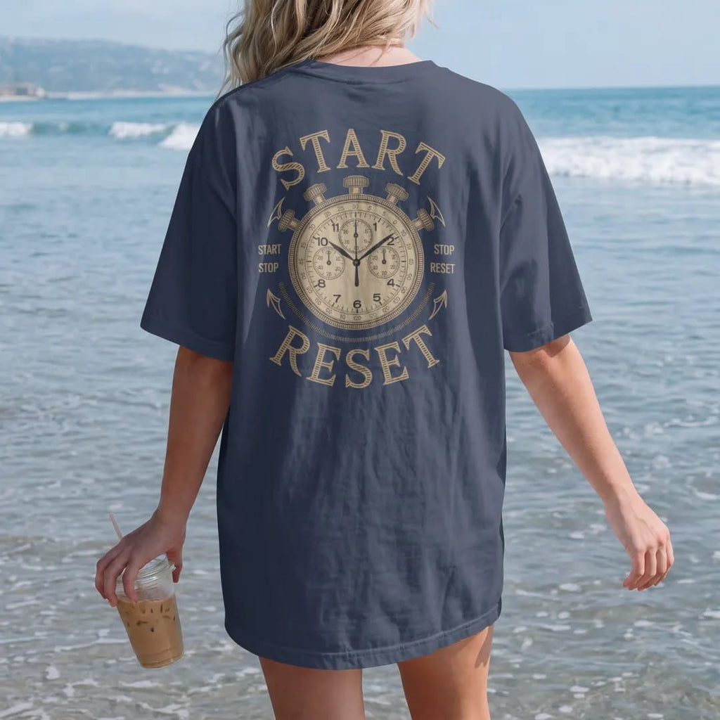 Woman on the beach in a Navy tee, back view: a chronograph watch with leader lines pointing to the pushers labeled Start, Stop and Reset, as a fine engraving in antique gold and cream.
