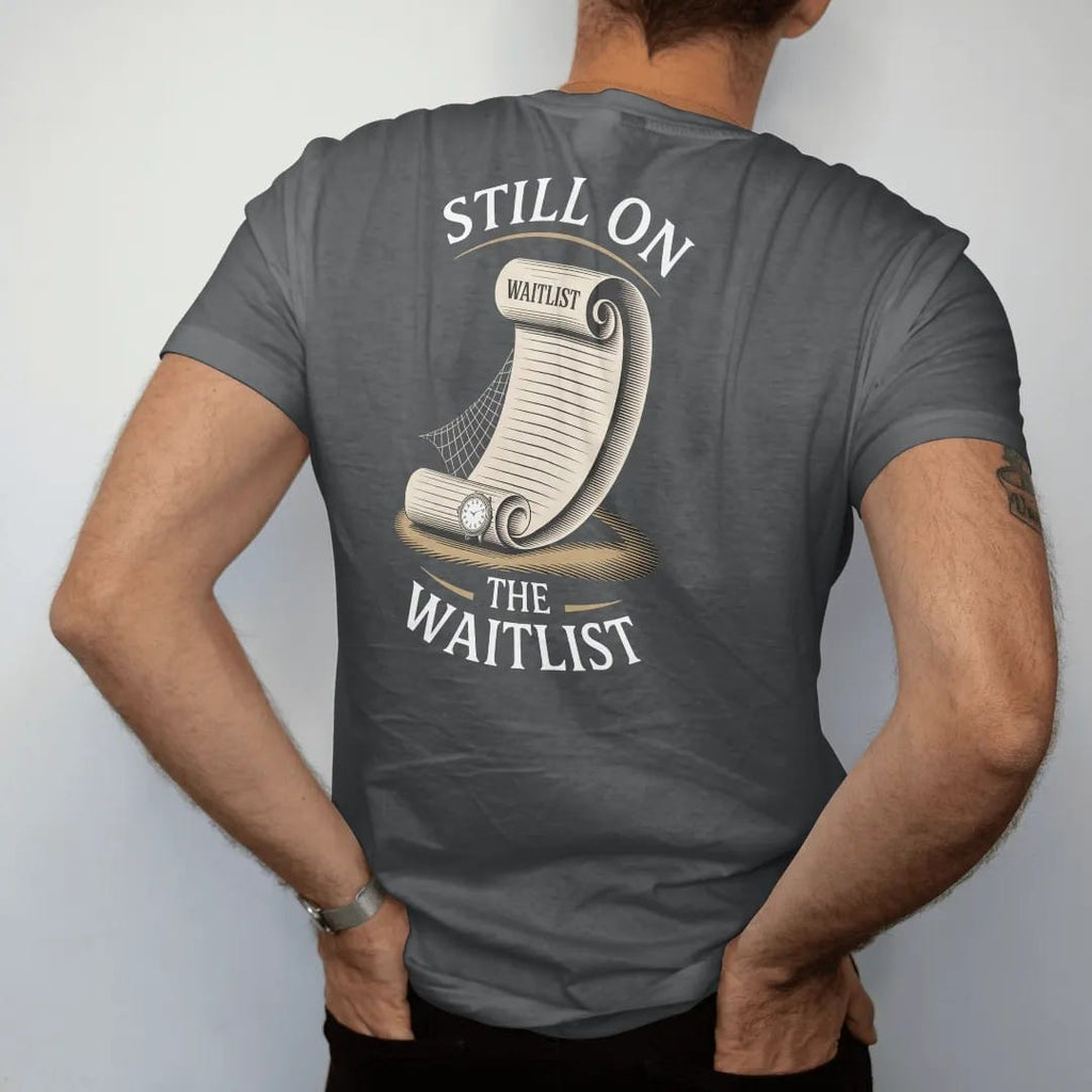 Man wearing a Graphite tee, seen from the back: a long waitlist scroll unrolling to a tiny watch and a cobweb, under Still On and The Waitlist, as a fine engraving in antique gold and cream.