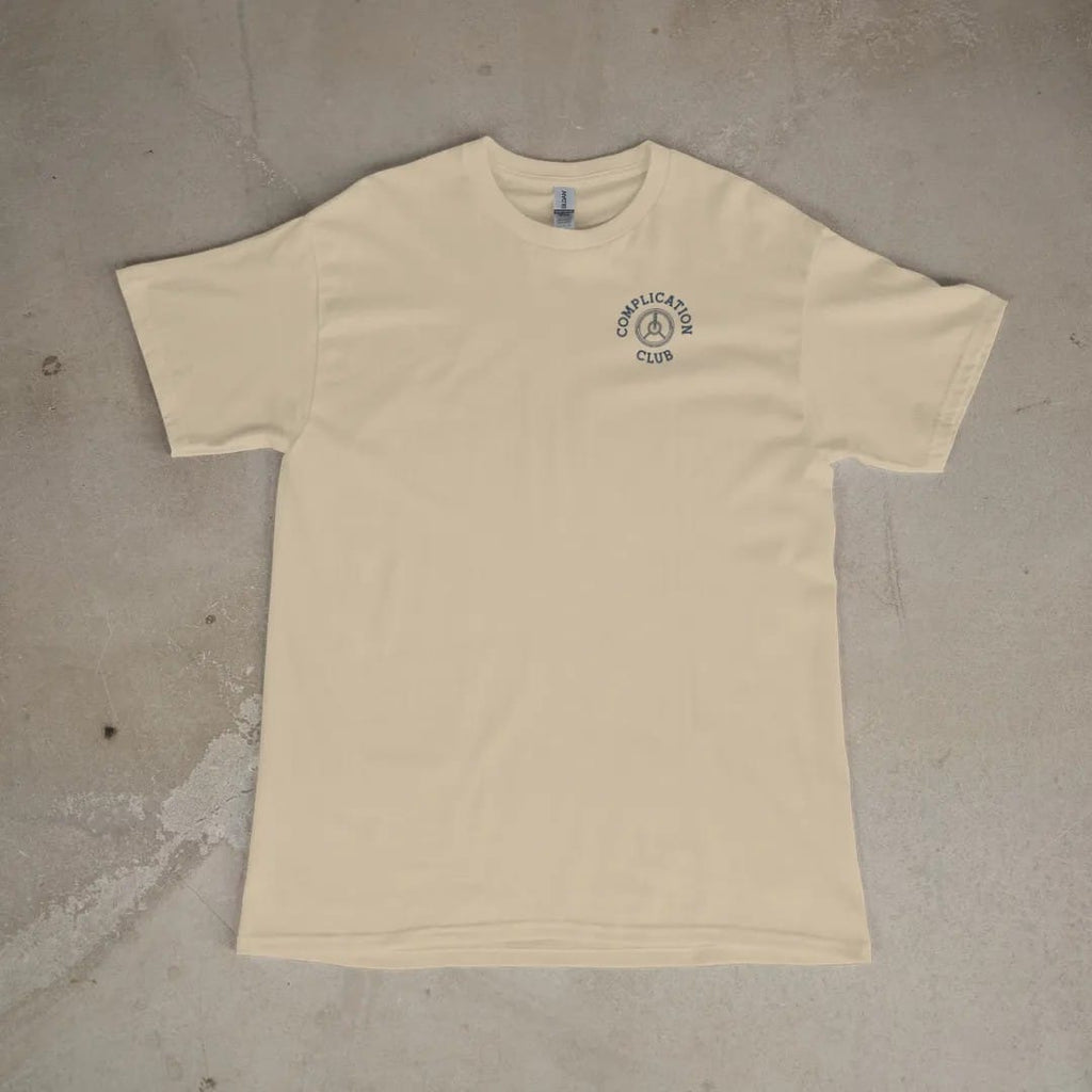 Front of a Sandstone tee laid flat, with the small Complication Club logo on the left chest.