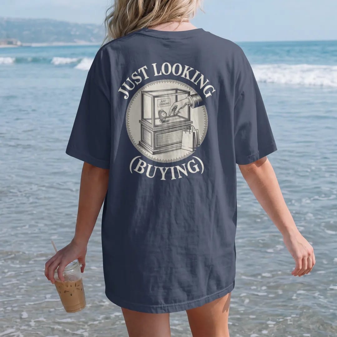 Woman on the beach in a Navy tee, back view: a boutique display case with a hand reaching for a watch and a small shopping bag, under Just Looking and a small (Buying), as a fine engraving in antique gold and cream.