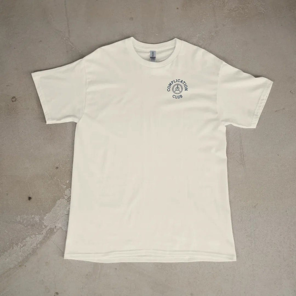 Front of a Ivory tee laid flat, with the small Complication Club logo on the left chest.