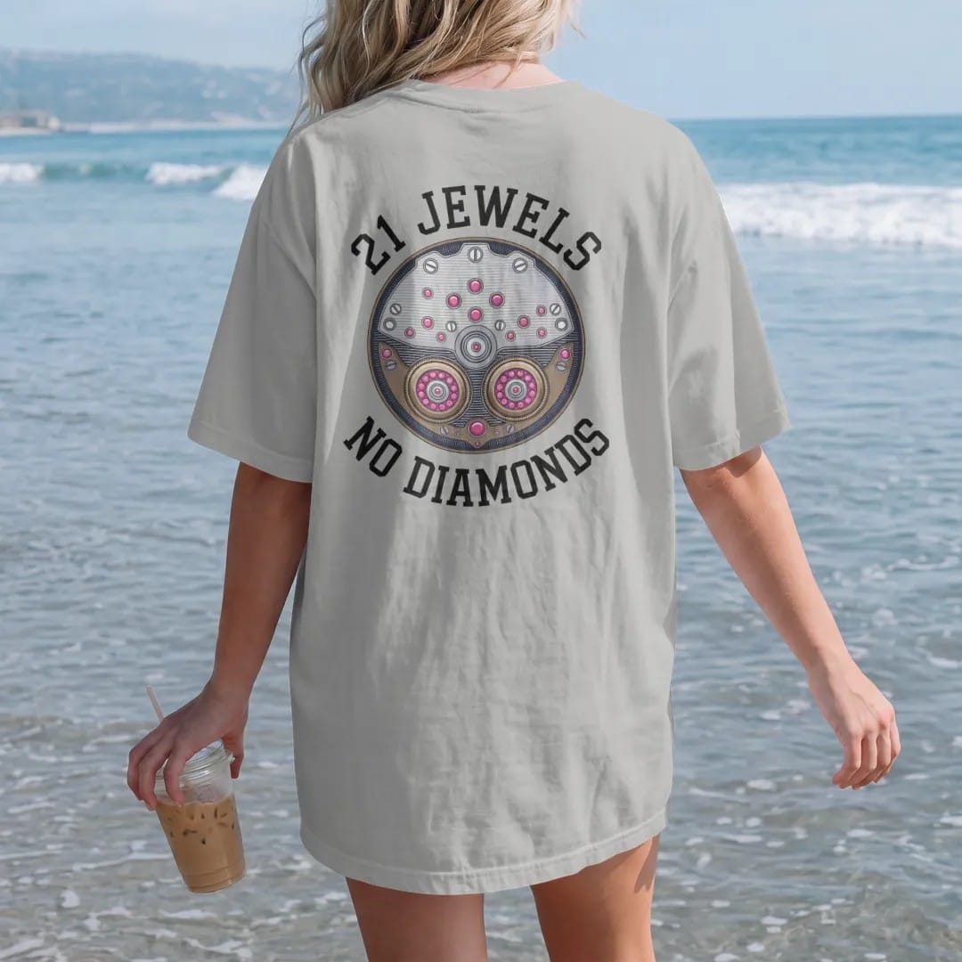 Woman on the beach in a Granite tee, back view: a movement plate with glowing ruby jewel bearings under 21 Jewels and No Diamonds, as a fine engraving in navy and antique brass.
