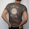 Man wearing a Espresso tee, seen from the back: a seconds hand with a smooth sweeping trail beside a crossed-out ticking hand, flanked by Sweep and Not Tick, as a fine engraving in antique gold and cream.