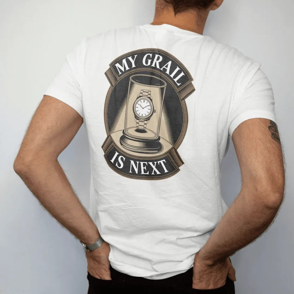 Man wearing a White tee, seen from the back: a glowing watch on a velvet pedestal behind glass with a rope and spotlight, under My Grail and Is Next, as a fine engraving in antique gold and cream.