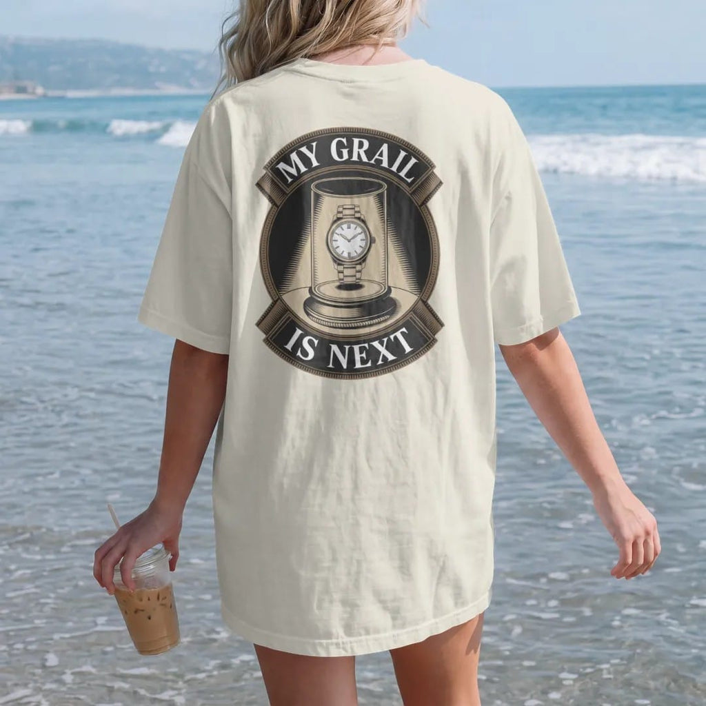 Woman on the beach in a Ivory tee, back view: a glowing watch on a velvet pedestal behind glass with a rope and spotlight, under My Grail and Is Next, as a fine engraving in antique gold and cream.