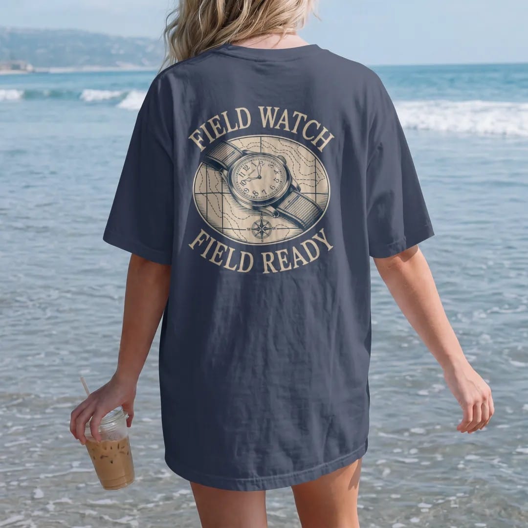 Woman on the beach in a Navy tee, back view: a rugged field watch on a canvas strap over a topo map with a compass, under Field Watch and Field Ready, as a fine engraving in antique gold and cream.